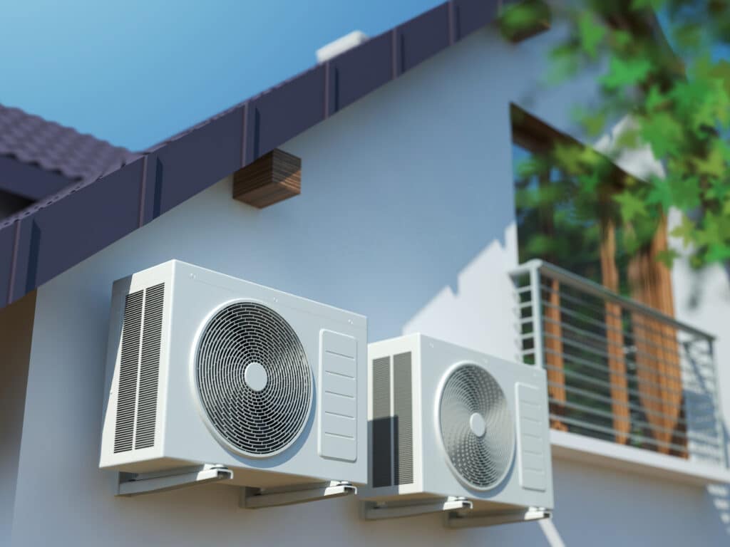 Deux climatiseurs blancs extérieurs fixés sur le mur clair d'une maison moderne sous un ciel bleu. Toit sombre et balcon.