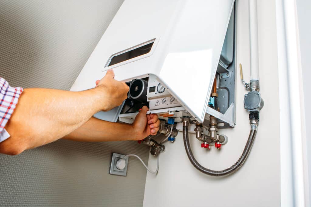 Plombier entretient une chaudière murale à gaz blanche. Ses mains ajustent les composants internes et la tuyauterie connectée.